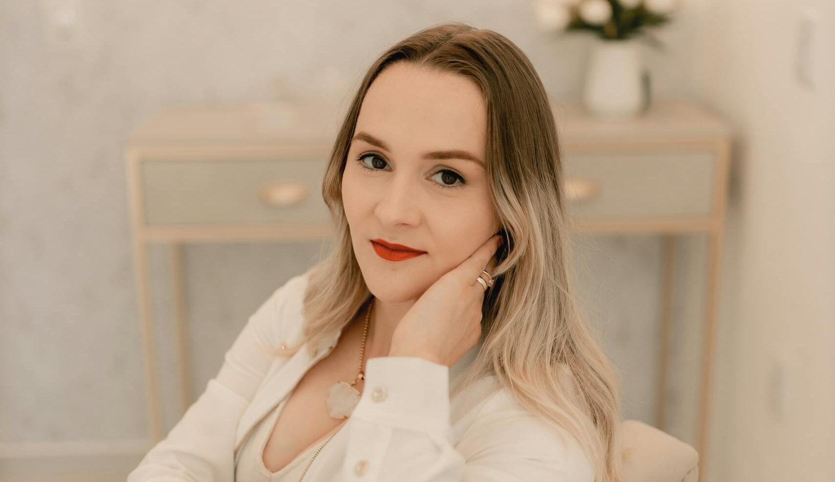 Stylish woman sitting in a modern, minimalist interior space with neutral tones.